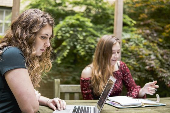 两名网上赌博平台(Chatham University)的学生坐在外面的一张小酒馆桌旁，用笔记本电脑独立学习. 