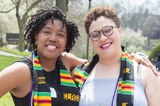 两名黑人妇女的照片, 网上赌博平台的毕业生, 穿着多元文化的毕业礼服，对着镜头微笑
