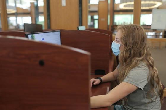 图为英国网上赌博平台的一名女学生戴着口罩，在图书馆的电脑前工作