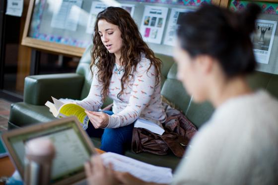 两名网上赌博平台女学生在图书馆工作的照片, 一个在看书，一个在看电脑