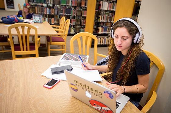 网上赌博平台的学生坐在珍妮·金·梅隆图书馆, 戴着耳机坐在桌子上学习，在电脑前工作. 