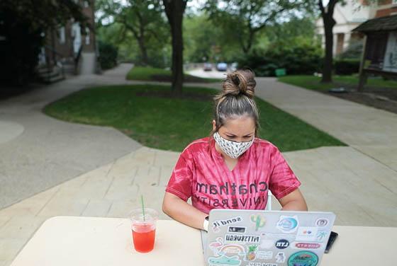 一名蒙面女学生身穿网上赌博平台衬衫的照片, 在网上博彩平台外用笔记本电脑工作