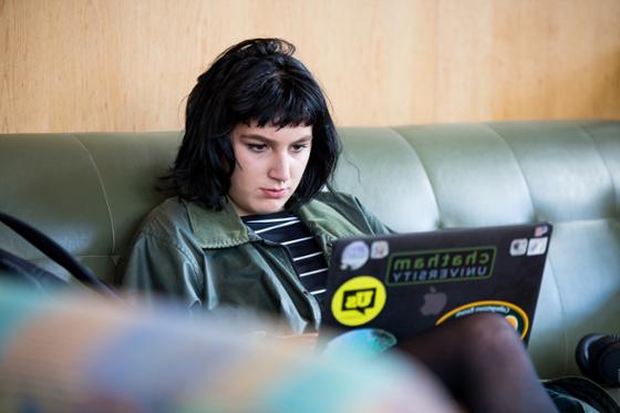 图为一位网上赌博平台的女学生坐在图书馆的沙发上, 在笔记本电脑上工作