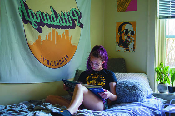 Photo of a female Chatham University student sitting on a bed in her dorm room reading