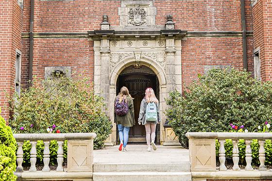 图为两名英国网上赌博平台女学生背着双肩包走进Shadyside校区的红砖建筑