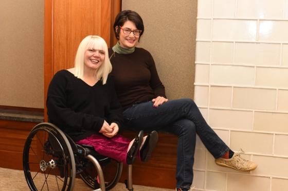 一个坐在轮椅上的女人和一个坐在轮椅扶手上的女人的照片，对着镜头微笑