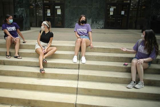 四名网上赌博平台学生的照片，戴着面具，坐在图书馆的台阶上