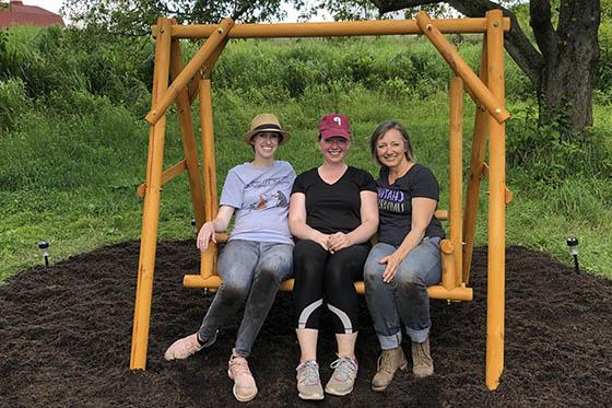 Photo of three women sitting on a swing bench in the Sensory Garden on Eden Hall Campus