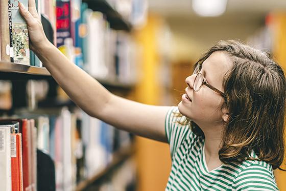 图为网上赌博平台的一名女学生从图书馆书架上取下一本书