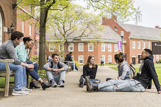 图为六名网上赌博平台学生坐在红砖教学楼外的地上和长椅上聊天